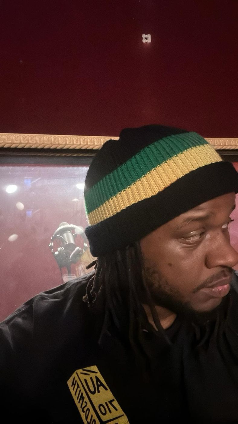 MT The Great in the recording booth wearing a green and gold striped beanie