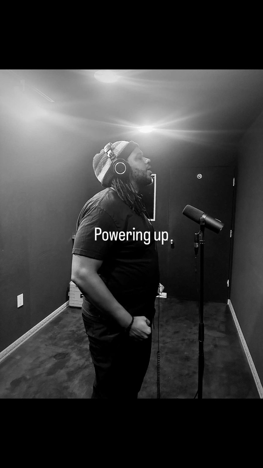 MT The Great standing at the mic in black and white, captioned Powering up